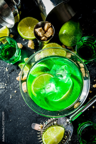 Strong alcohol cocktail. Absinth and vodka martini drink with sugar, ice cubes and lime, With ingredients, barmen utensils and shot glasses with absinthe. Dark stone background copy space