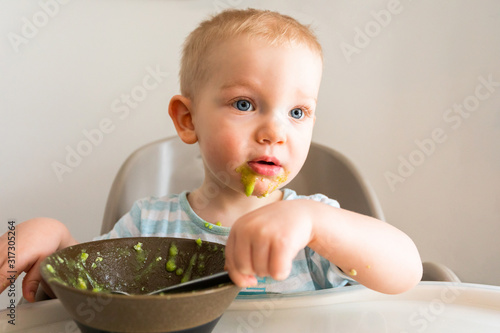 Little boy alone eats puree from a plate.