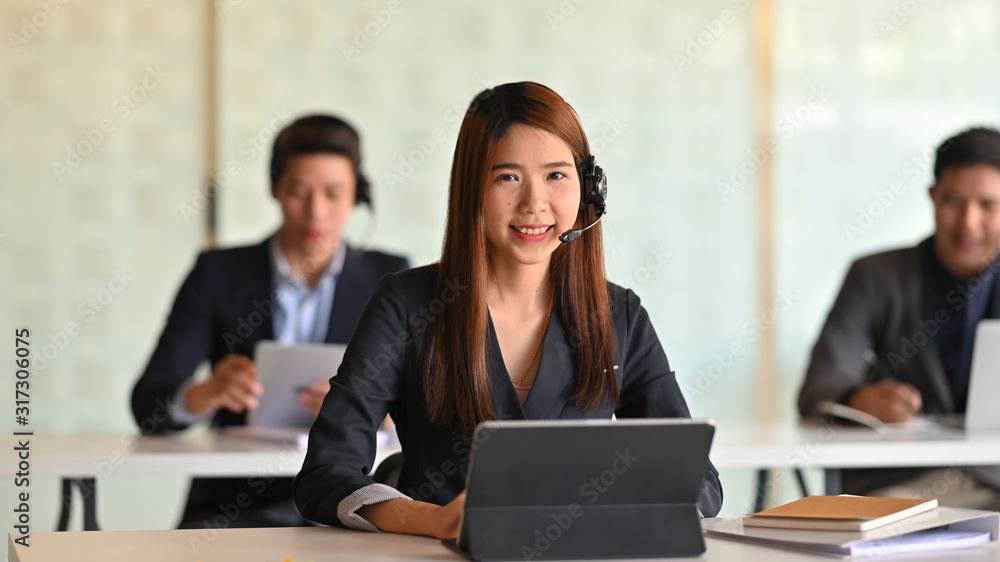 Beautiful woman with headset , look good in black suit working as call-center surrounded by her colleague at the modern office. Beautiful woman with headset , look good in black suit working as call-center surrounded by her colleague at the modern office.