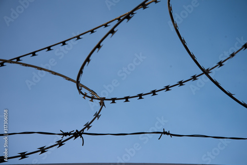 Beautifully curved barbed wire against the blue sky. Close up.