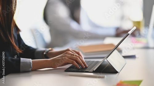 Cropped shot of business woman hand while typing on computer tablet and sitting next to her colleague.
