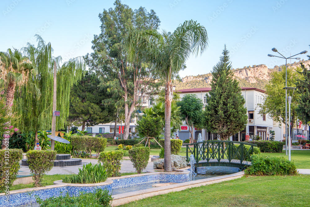Green city park with palm trees and a fountain on a sunny day, Kemer, Turkey