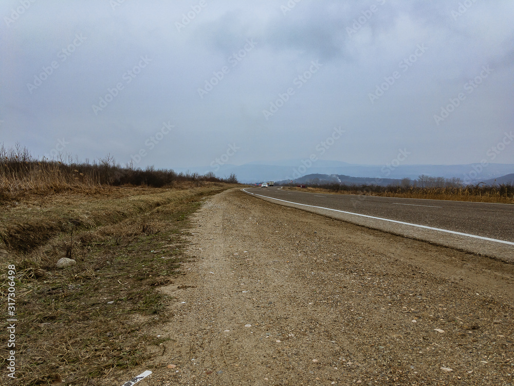 The roadside runs along a plain with mountains in the distance with haze in cloudy weather in winter without snow. The roadside runs along a plain with mountains in the distance with haze in cloudy weather in winter without snow.