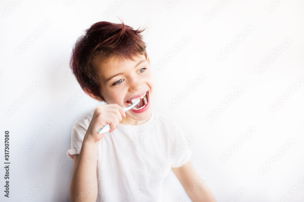 Horizontal portrait of smiling child brushing teeth with blue and white toothbrush and looking away. Dental and health care from childhood. Healthy teeth on smiling face. White background. Copy space Horizontal portrait of smiling child brushing teeth with blue and white toothbrush and looking away. Dental and health care from childhood. Healthy teeth on smiling face. White background. Copy space