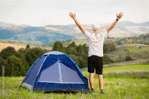 Young man with hands up camping tent facing amazing views of mountain