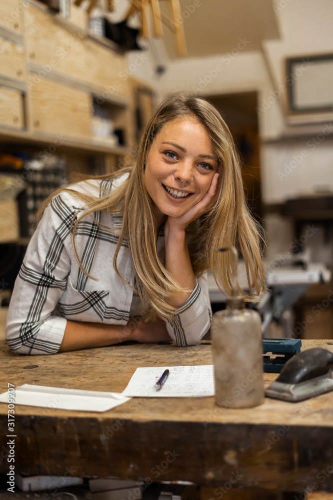 Portrait of smiling young woman with head in hands sitting in workshop Portrait of smiling young woman with head in hands sitting in workshop