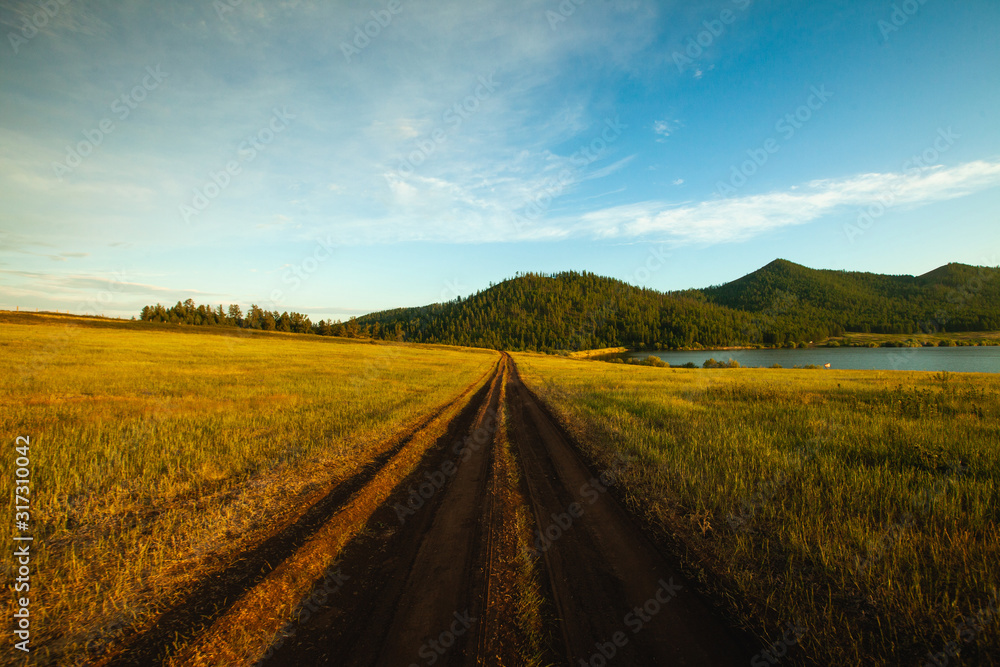 Dirt road passing through grassy landscape with mountains in background, Siberia, Russia Dirt road passing through grassy landscape with mountains in background, Siberia, Russia