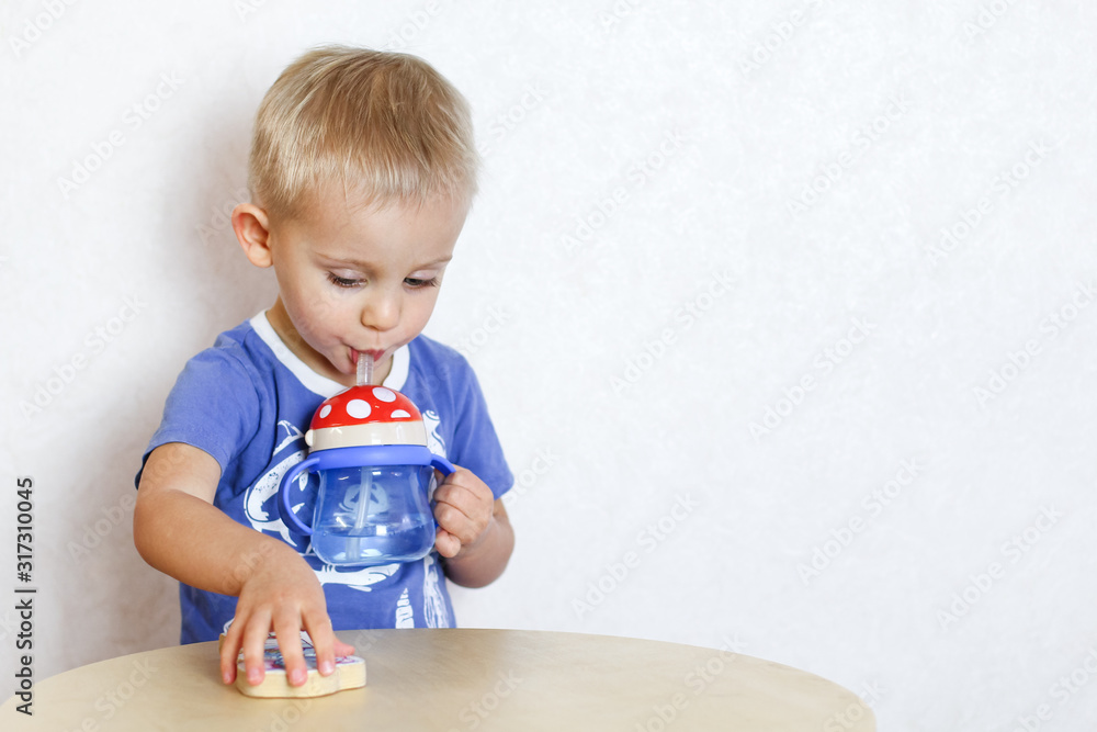 Blonde Toddler boy drinking water from a drinker with a straw Blonde Toddler boy drinking water from a drinker with a straw