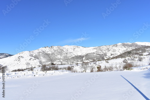 Winter landscape with snowy white field, trees, mountains covered with snow and blue sky. Piornedo village, Ancares, Lugo, Galicia, Spain.