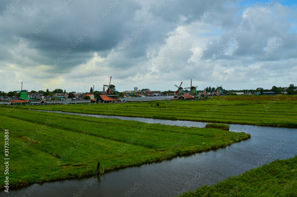 Zaanse Schans, Holland, August 2019. North-east of Amsterdam is a small community located on the quay of the Zaan river. View from above of the fields with mills, tourists are noticed. Cloudy day.