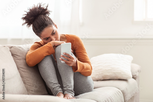 Valokuvatapetti Depressed Afro Lady Holding Mobile Phone Sitting On Sofa Indoor