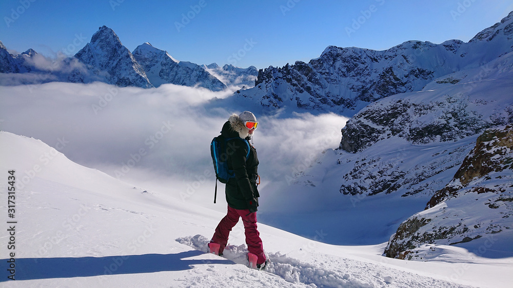 Cheerful female snowboarder poses on the snowy mountaintop before her descent Cheerful female snowboarder poses on the snowy mountaintop before her descent