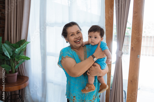 Grandma stand with carrying little grandson wearing casual clothes at home © Odua Images