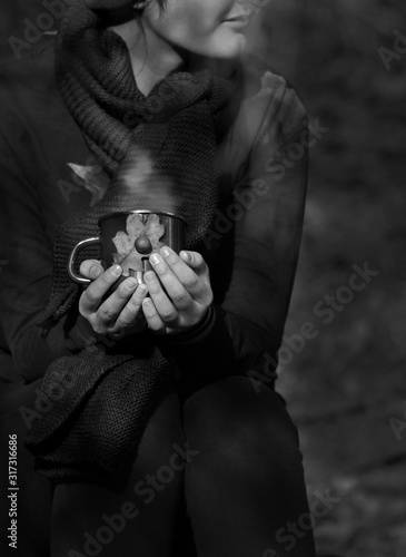 Black and white portrait, girl holds a hot mug of drink in her hands outdoors 