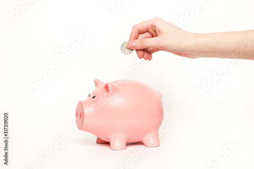 A pink pig piggy bank is standing on a white background and is putting a coin inside with his hand. Savings and Finance