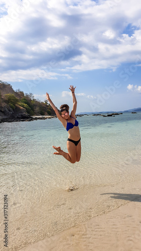 A girl in bikini jumping on a white sand beach and a shallow bay water in Komodo National Park, Indonesia. She is enjoying her time and have fun. Idyllic, isolated beach. Roaming free. Jump of joy