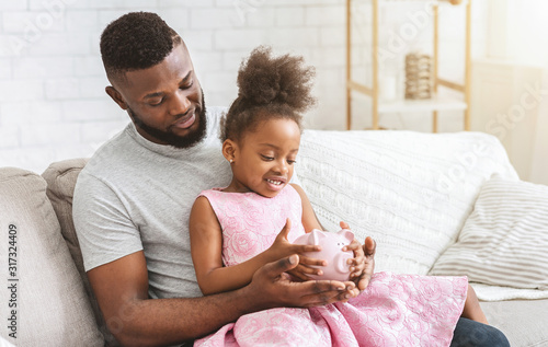 Young afro father showing little daughter piggy bank photo