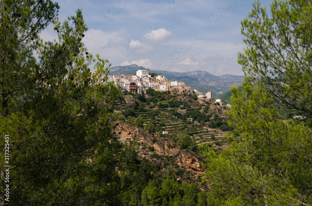 Among the trees a view of the village Lucena del Cid surrounded by nature on a day with blue sky and clouds, Castellón, Spain Among the trees a view of the village Lucena del Cid surrounded by nature on a day with blue sky and clouds, Castellón, Spain