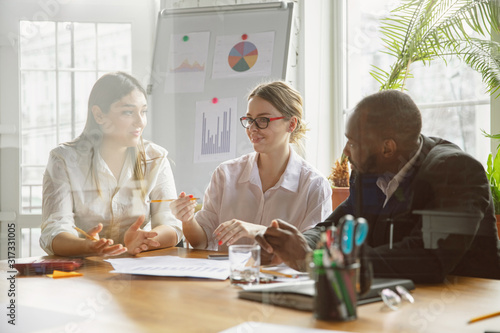 Modern work. Group of young business professionals having a meeting. Diverse group of coworkers discuss new decisions, plans, results, strategy. Creativity, workplace, business, finance, teamwork.