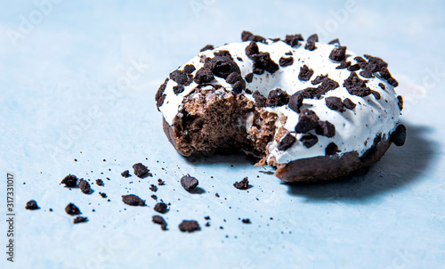 one delicious fresh hearty black and white bitten donut lie on a blue background. jank food and high-calorie food photo