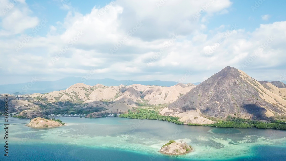 A drone shot of a paradise island with some boats anchored around in Komodo National Park, Flores, Indonesia. Green middle part of the island turns into white sand beach and further into turquoise sea