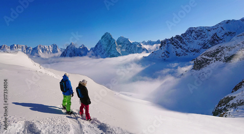 COPY SPACE: Snowboarders stand atop a mountain and observe the snowy mountains.