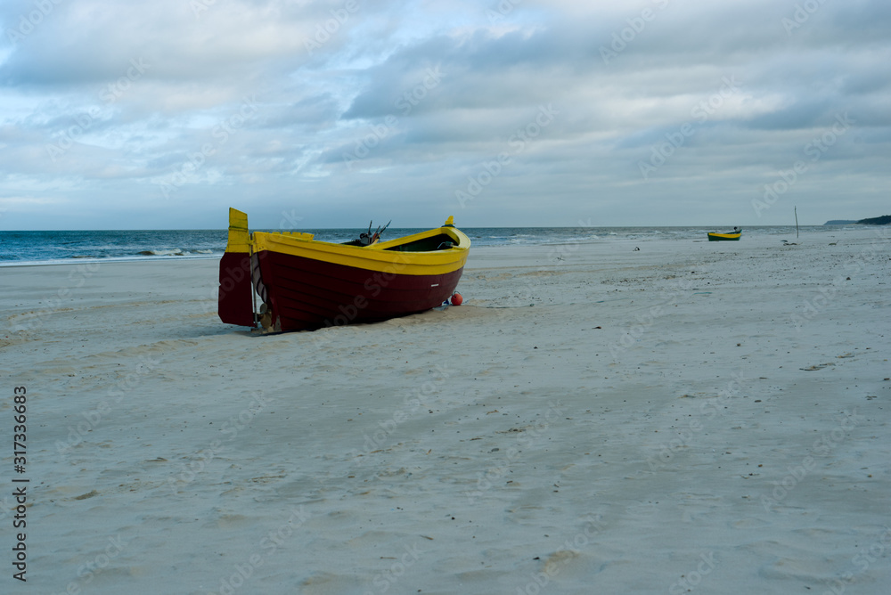 A maroon yellow maritime cutter stands on the beach in the sand