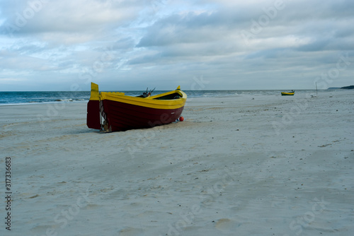 A maroon yellow maritime cutter stands on the beach in the sand