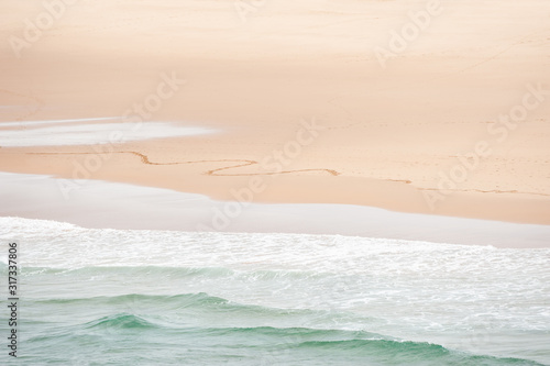 Waves on the beach and traces on the sand. Top view. Shore of Atlantic ocean in Algarve, Portugal. Abstract sea background