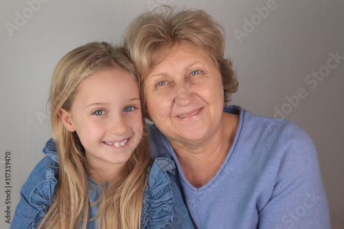 Portrait of 2 happy blonde grandmother and granddaughter with blue eyes and blue clothes, close up