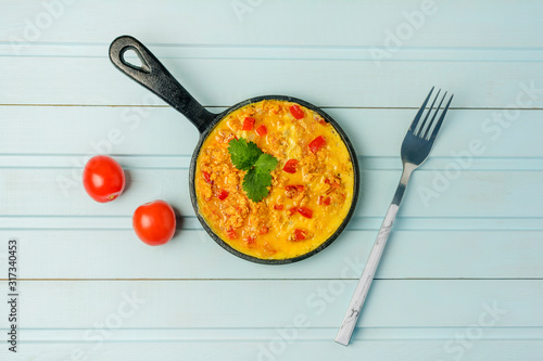 Freshly made omelet from eggs and vegetables. Turkish national recipe Menemen with eggs, bell pepper and tomatoes. Photo on a blue background with copy space.