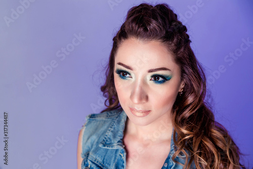 Beautiful brunette girl with blue makeup, pigtails and loose curly hair on a purple background