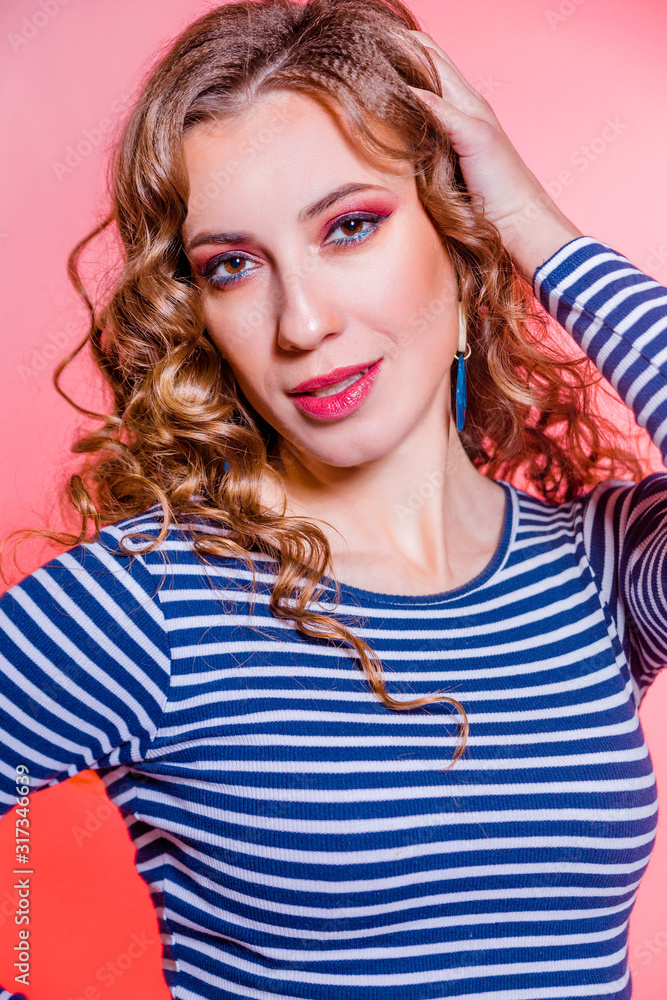 Happy beautiful brunette girl with red makeup, curly hair and a blue stripes sweater posing against a red background. Happy beautiful brunette girl with red makeup, curly hair and a blue stripes sweater posing against a red background.