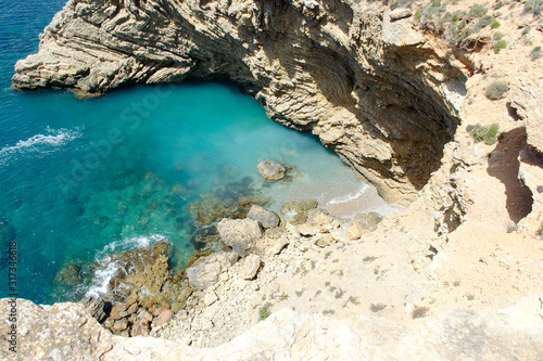 Rocky sea coast with clean blue water, cloudy sky and city view. Ibiza island, Spain