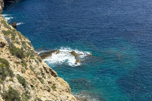 Rocky sea coast with clean blue water, cloudy sky and city view. Ibiza island, Spain