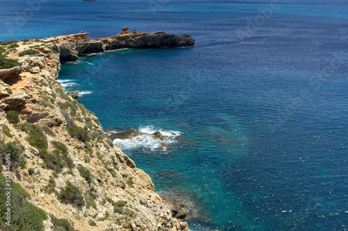 Rocky sea coast with clean blue water, cloudy sky and city view. Ibiza island, Spain