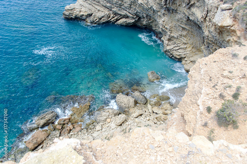 Rocky sea coast with clean blue water, cloudy sky and city view. Ibiza island, Spain
