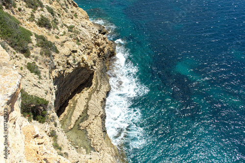 Rocky sea coast with clean blue water, cloudy sky and city view. Ibiza island, Spain