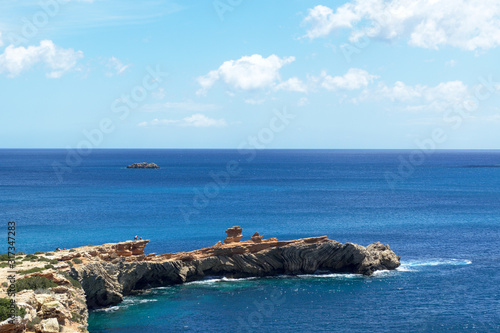 Rocky sea coast with clean blue water, cloudy sky and city view. Ibiza island, Spain