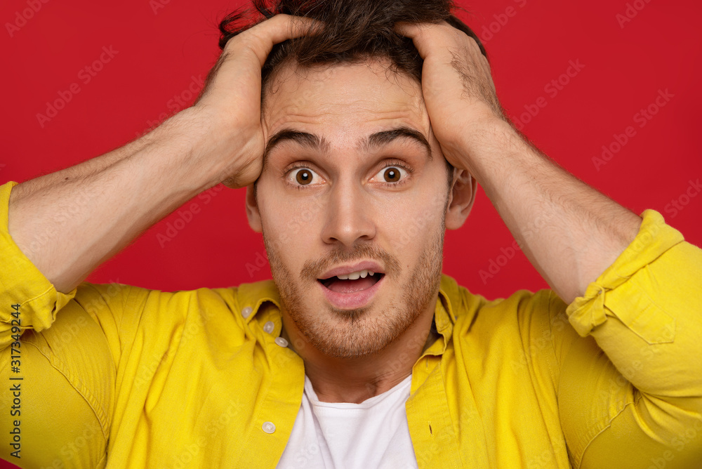 crazy man in yellow shirt holding head and looking at camera isolated on red background crazy man in yellow shirt holding head and looking at camera isolated on red background