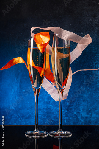 Two glasses with champagne on a black mirror surface. Flying satin ribbon. Blue background Concrete wall. Black glass. Crystal glass