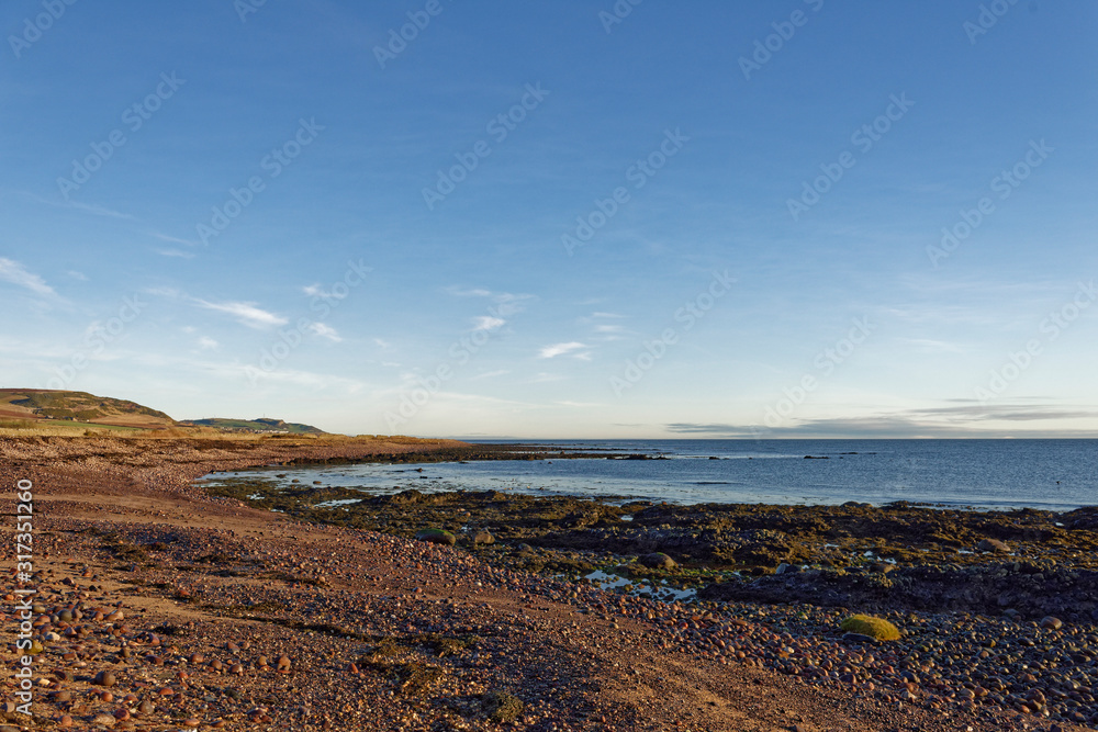 The Shingle and rocky beach seen beside the coastal footpath between Johnshaven and Inverbervie at low tide on a clear sunny January Morning,