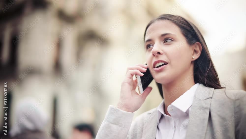 Attractive and cheerful businesswoman using smartphone in a crowded street. She is talking on the phone and laughing. Attractive and cheerful businesswoman using smartphone in a crowded street. She is talking on the phone and laughing.