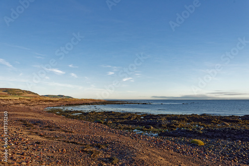The Shingle and rocky beach seen beside the coastal footpath between Johnshaven and Inverbervie at low tide on a clear sunny January Morning,