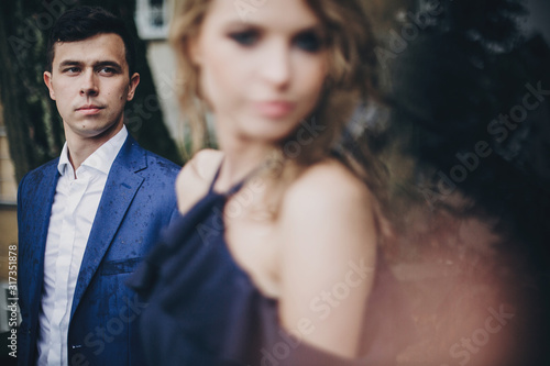 Portrait of stylish couple embracing in rainy european city street. Sensual romantic moment. Fashionable man and woman in love posing with passionate look. Valentines day