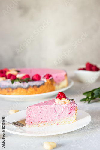 Raspberry cream mousse cake (no baked cheesecake) decorated with fresh raspberries, mini cookies and coconut flakes on light grey background.