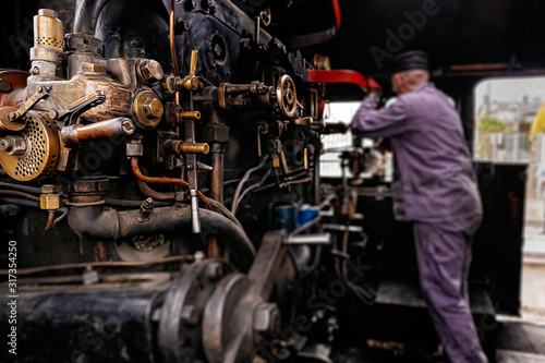 Selective focus on steam engine elements or parts in steam train cabin with blurred engineer or train driver working on cranks, Ireland