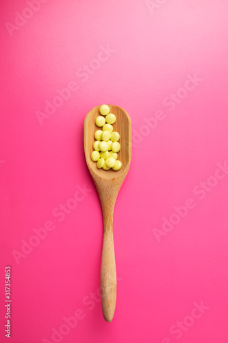 Natural supplement for health and beauty. Flatlay bamboo spoon with yellow tablets on pink background
