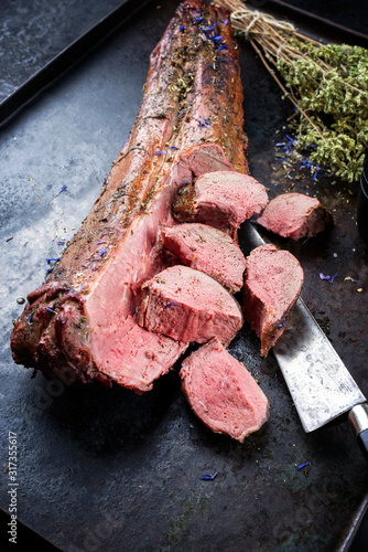 Barbecued dry aged venison tenderloin fillet steak and saddle natural with herbs offered as closeup on a rustic metal tray photo