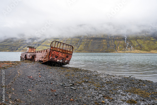 Rusty and abandoned old ship wreck from world war two laying on land in Mjoifjordur in Iceland. Waterfalls and foggy landscape scenery. Transport and ship concept. photo